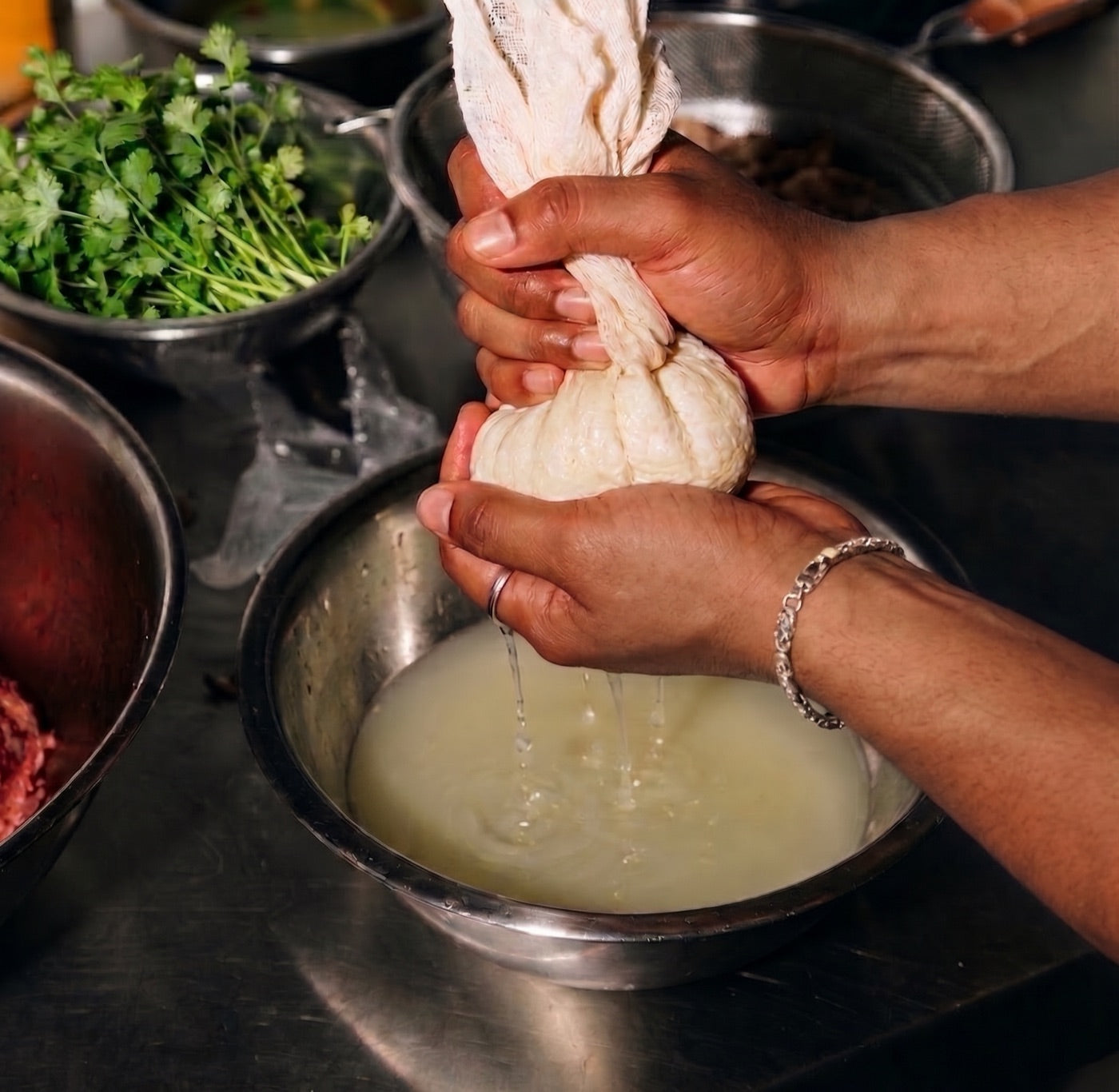Hands pressing fresh paneer through cheesecloth, whey dripping into a steel bowl